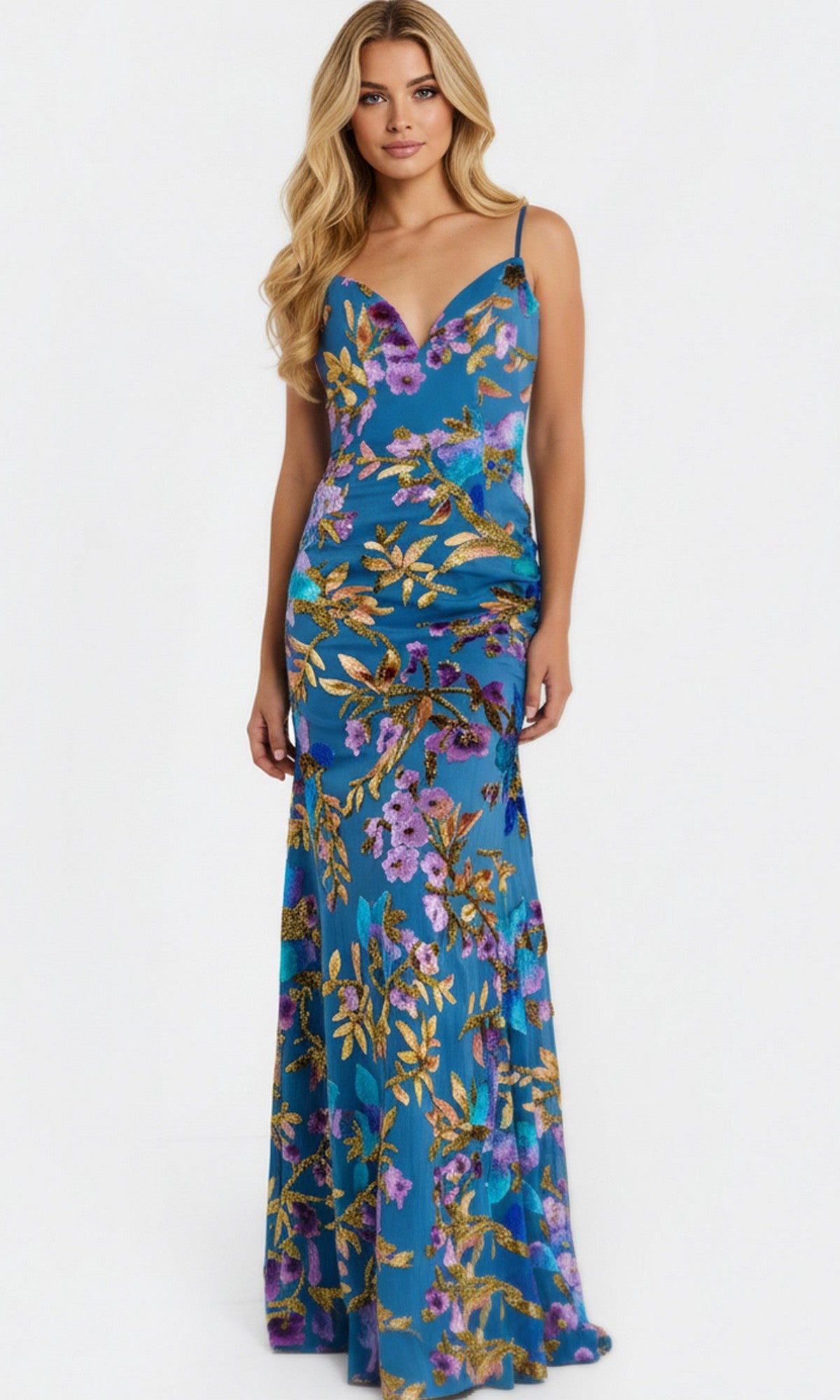 A woman wearing the Jovani 47655 long prom dress—blue with a floral pattern, thin straps, and a deep V-neckline—stands against a plain white background.